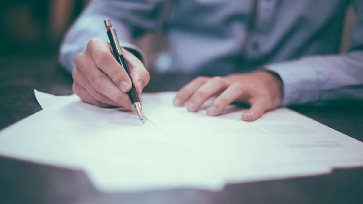A hand signing a printed document on a desk