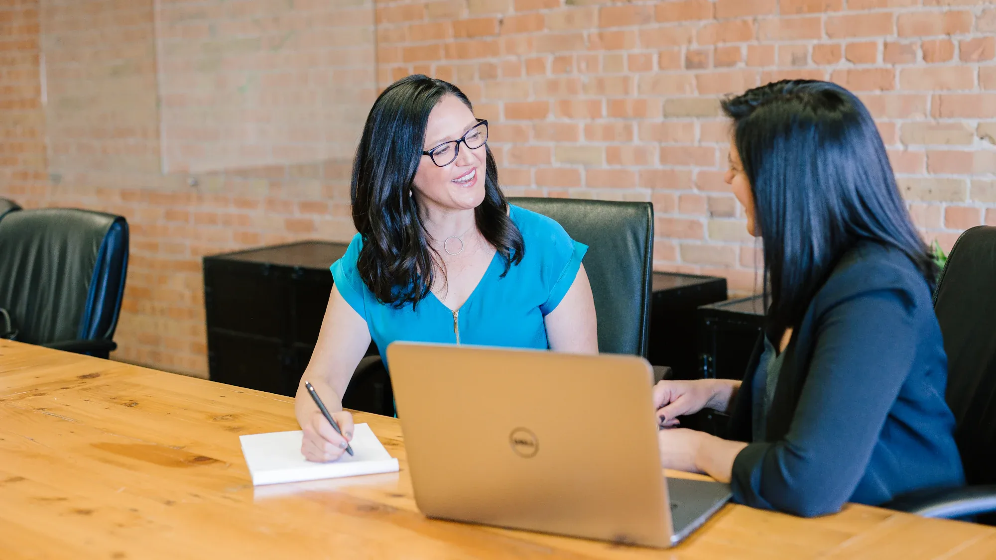 Two colleagues talking across a table with a laptop