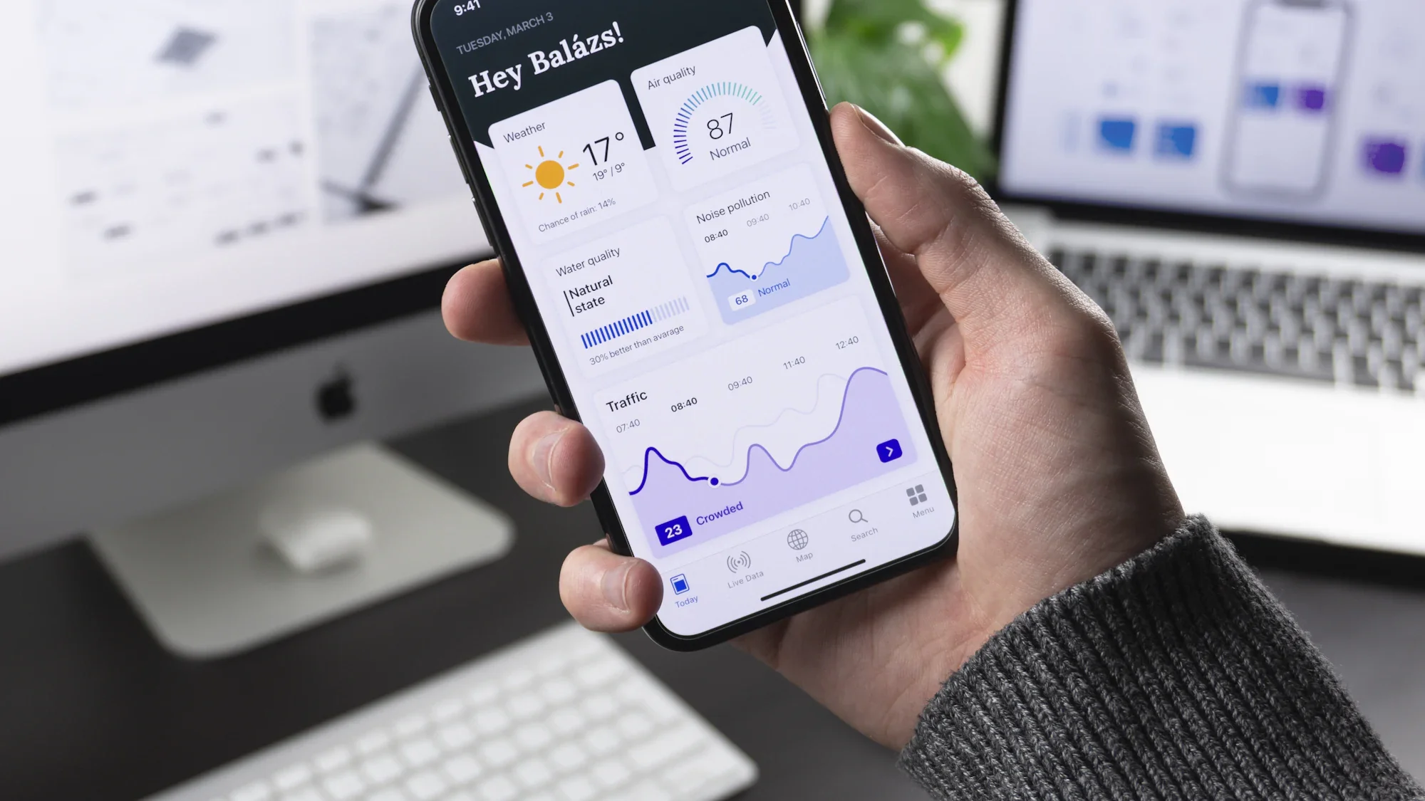 A hand holding a phone showing an analytics app in front of a laptop