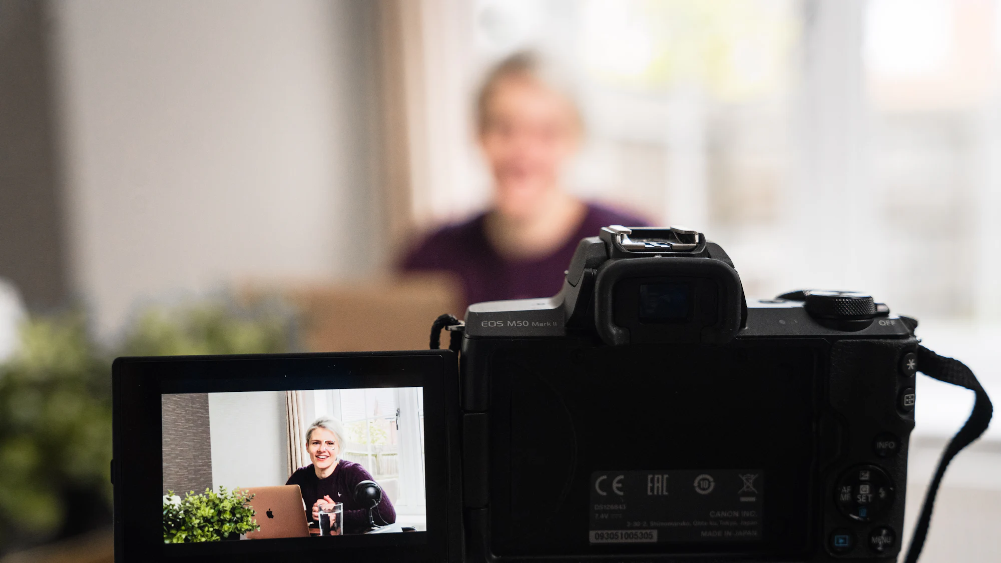 A camera's screen framing a creator as she films at a desk