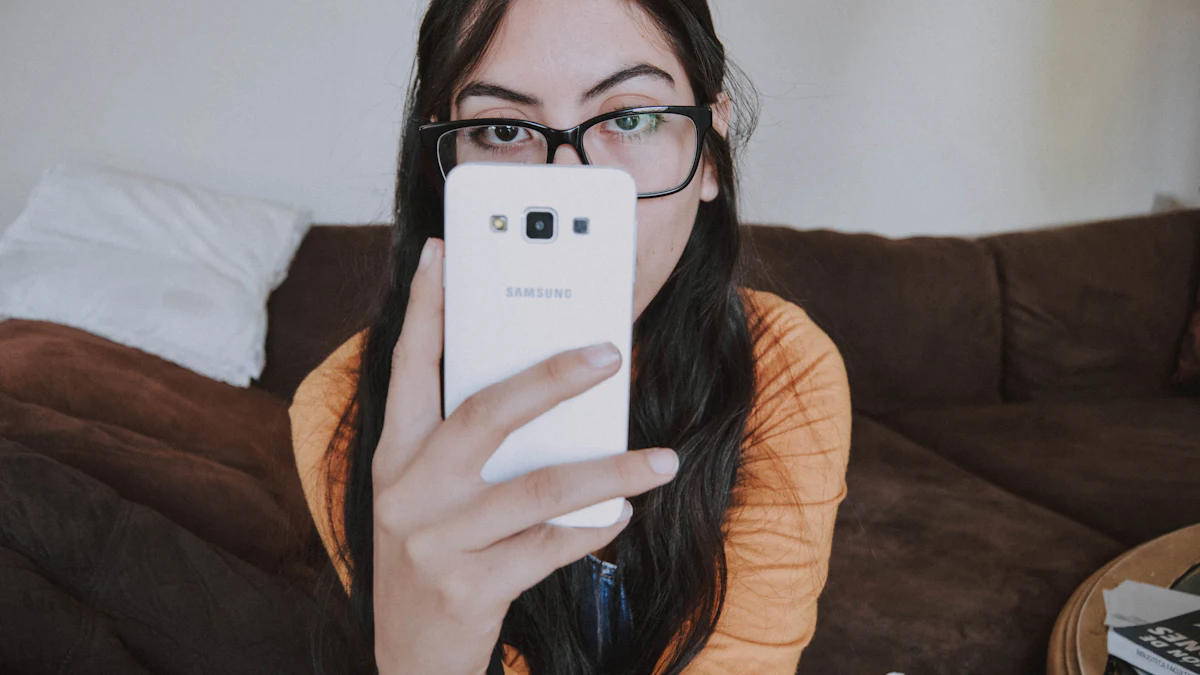 A woman in glasses on a sofa holding a white phone up in front of her face