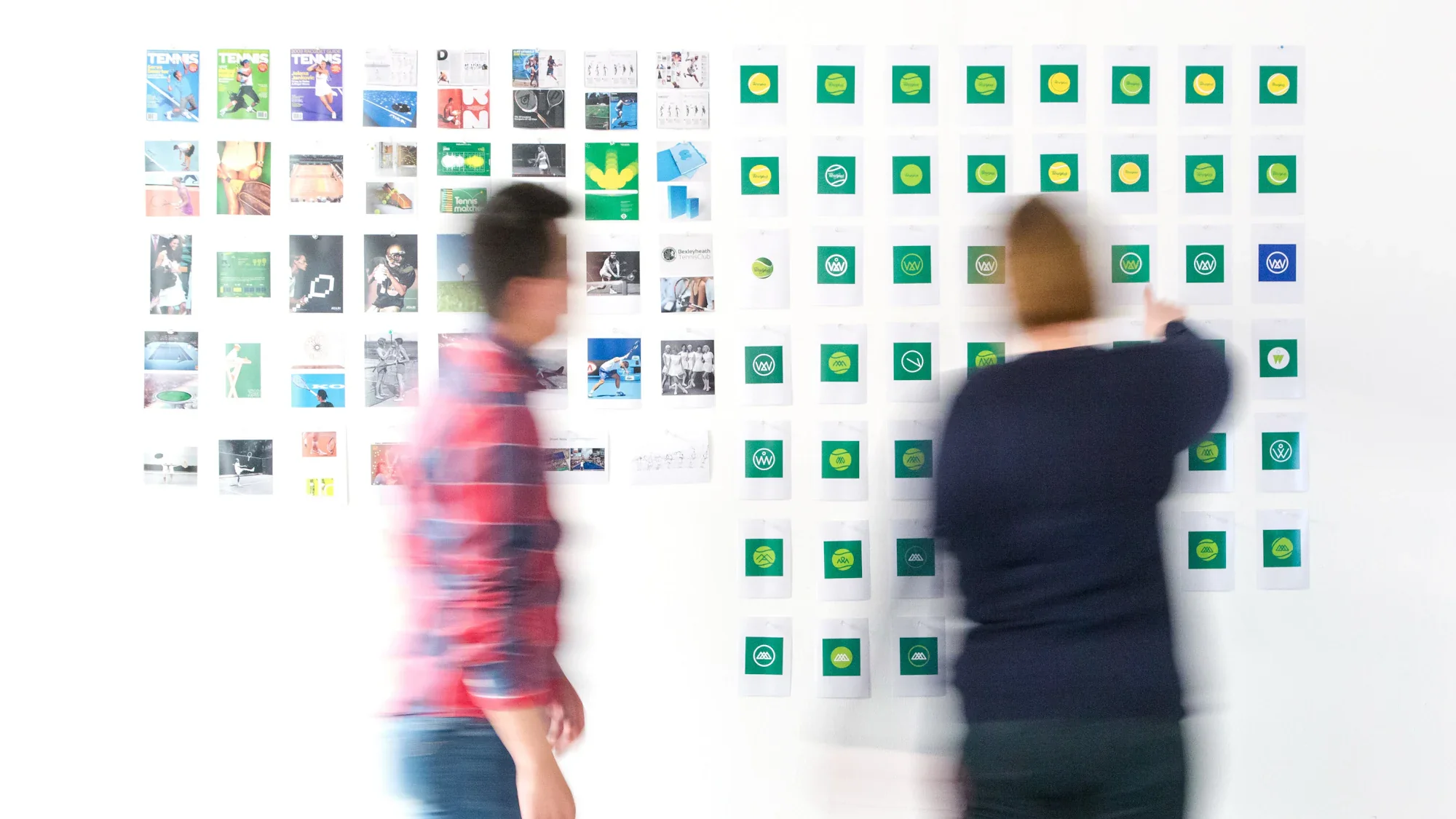 Two people arranging pictures on a large white wall