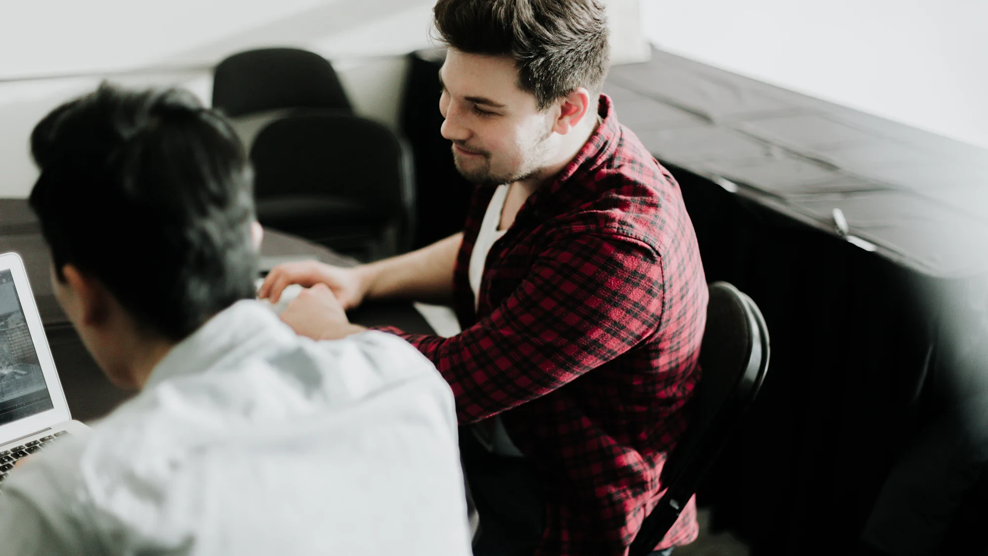 Two people shaking hands across a desk with a laptop