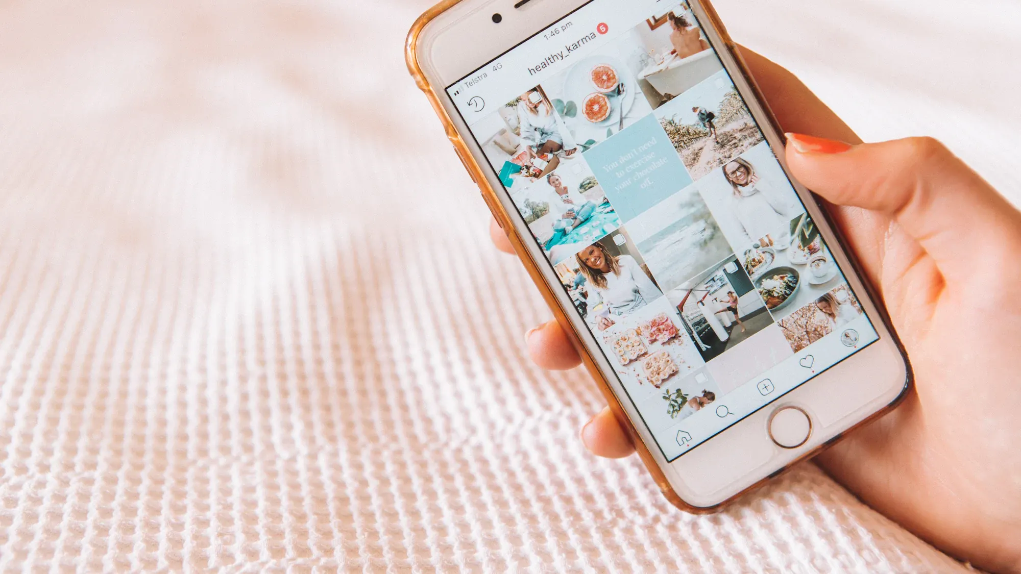 A hand holding a phone showing a grid of photos on a profile
