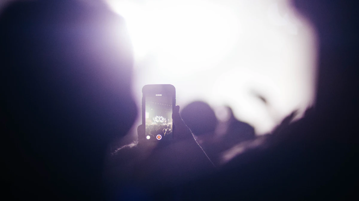 A phone held up to record a stage, its screen glowing in a dark crowd