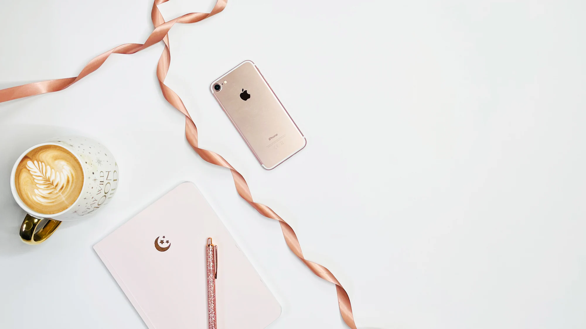 A flat lay of a phone, a coffee and a ribbon on a white desk