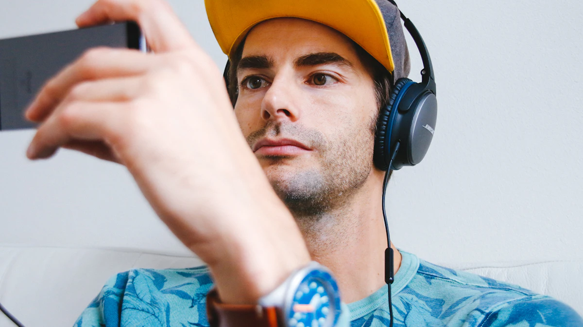 A man in headphones and a yellow cap watching a phone held up in front of him